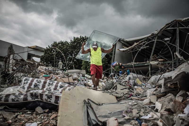 Jonaton retrieves an unbroken sheet of glass from a collapsed store to help him rebuild his home in Portoviejo.