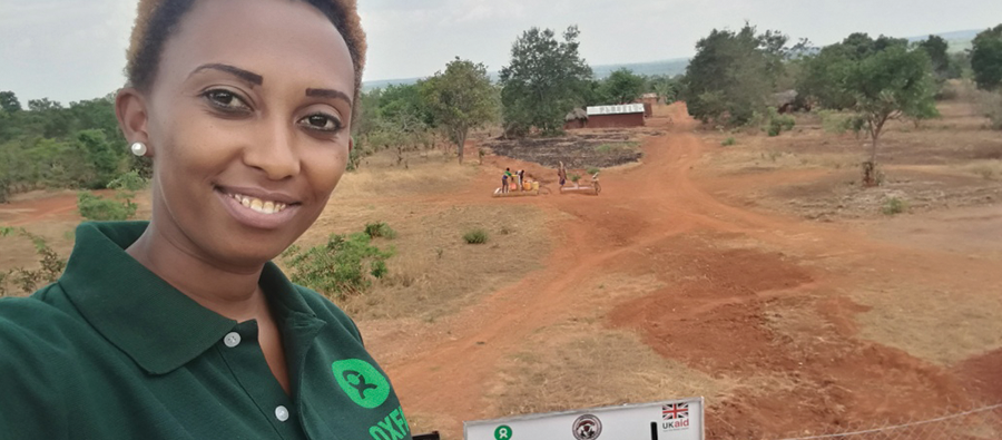 Gloria, a young woman standing with a green Oxfam short in a rural village