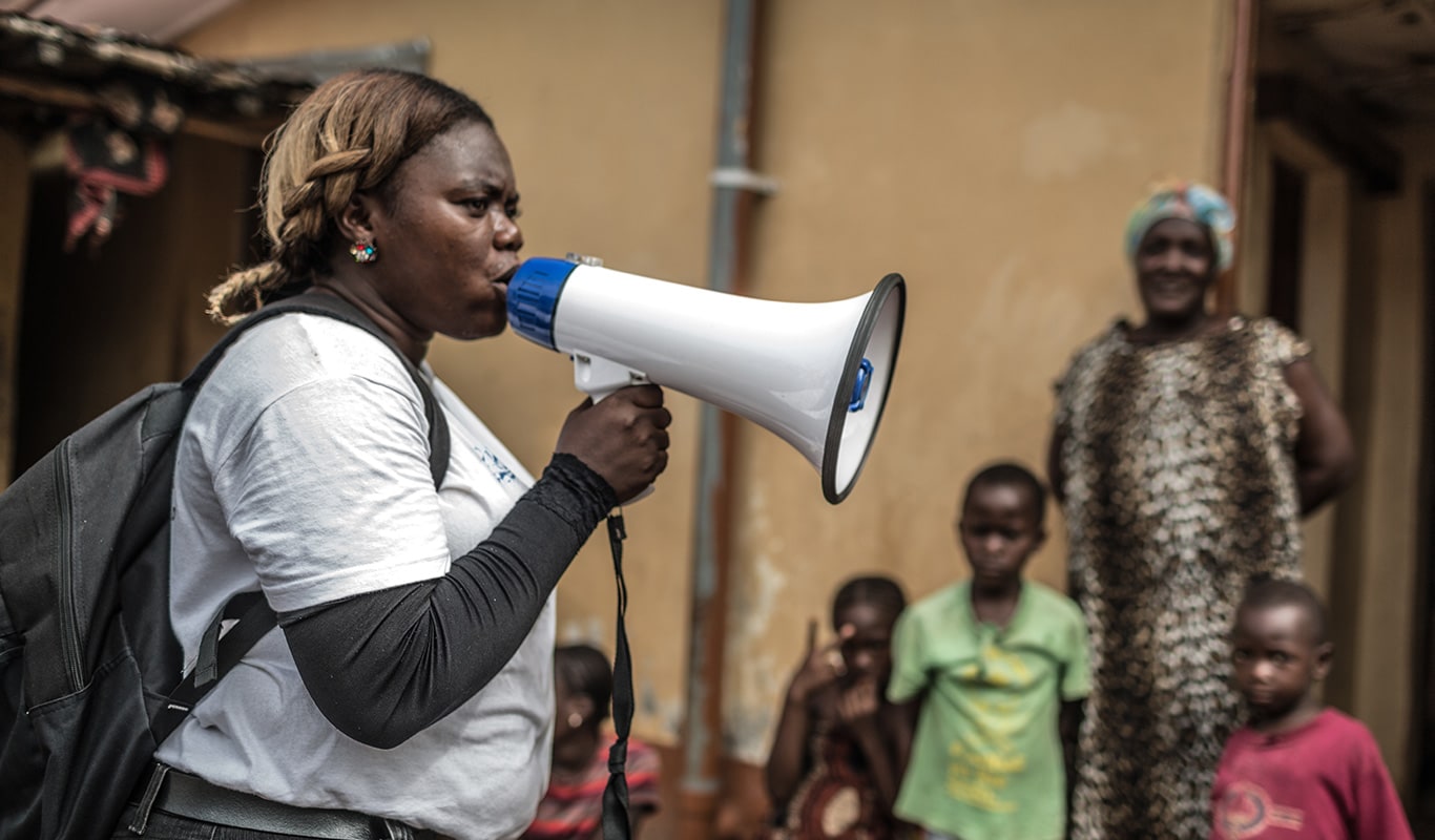 Woman with a megaphone speaks to a crowd about Ebola prevention