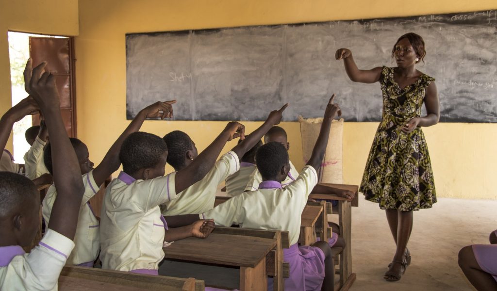 A teacher in Northern Ghana stands in front of a classroom of girls who all have their hands up.