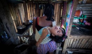 A woman carries a toddler in her back.