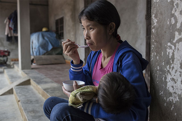 Lan crouching holding an infant and eating from a bowl