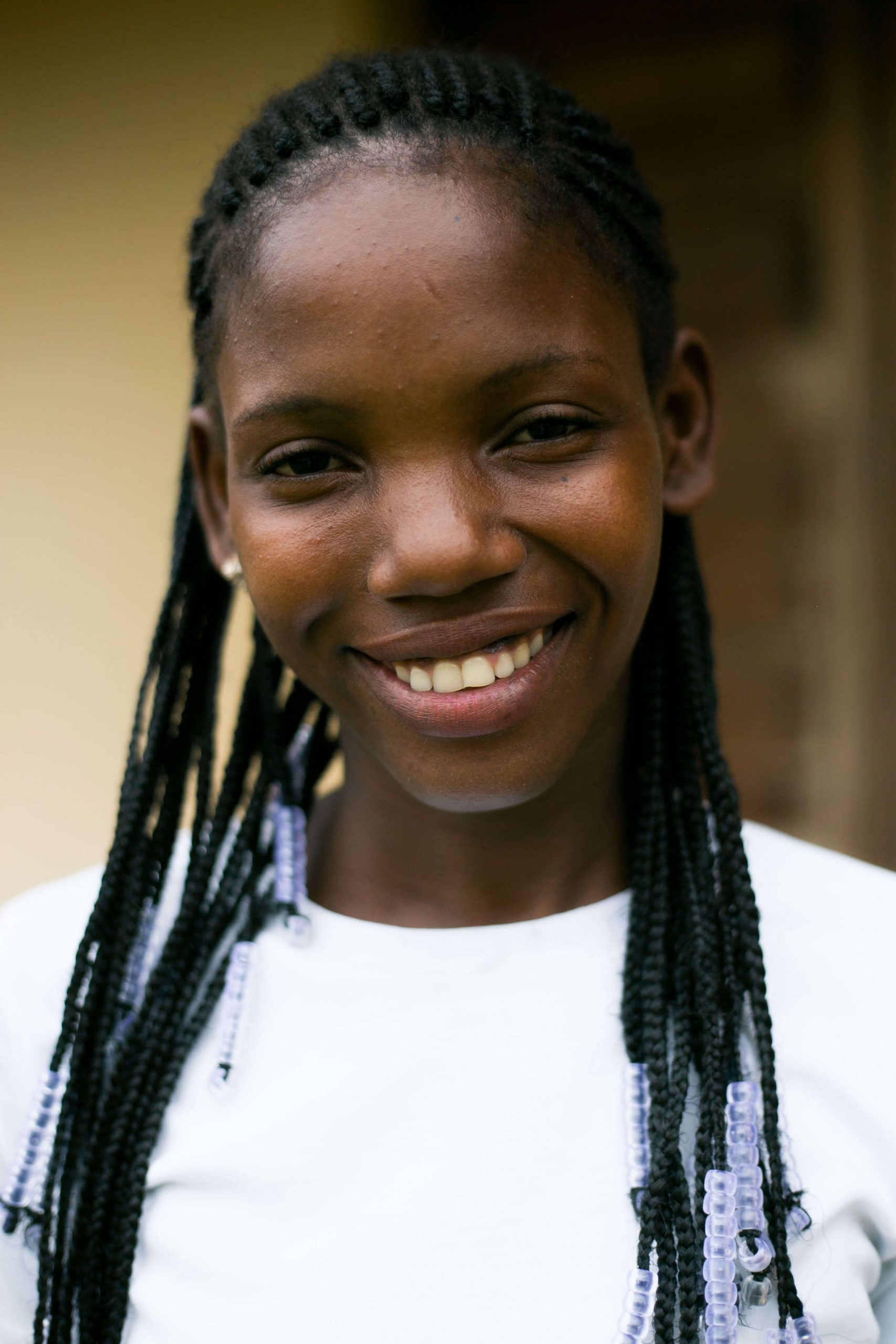 Portrait of a Black girl wearing a white shirt, smiling while looking directly at the camera.