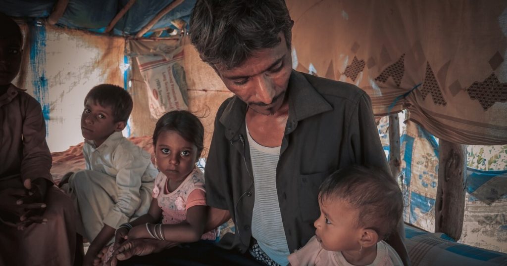 A yemeni man sits on a bed with three of his young children.