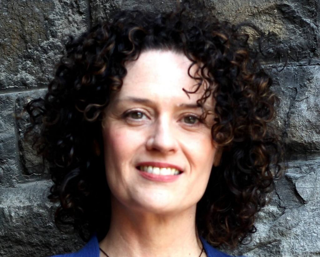 An image of a woman with shoulder length curly hair smiling and looking at the camera