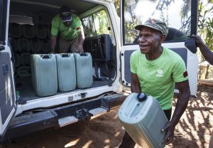 A man in a green Oxfam t-shirt carrying equipment out of a truck