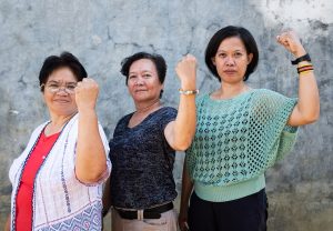 Three woman, raising their fists in a show of strength and partnership against a concrete wall