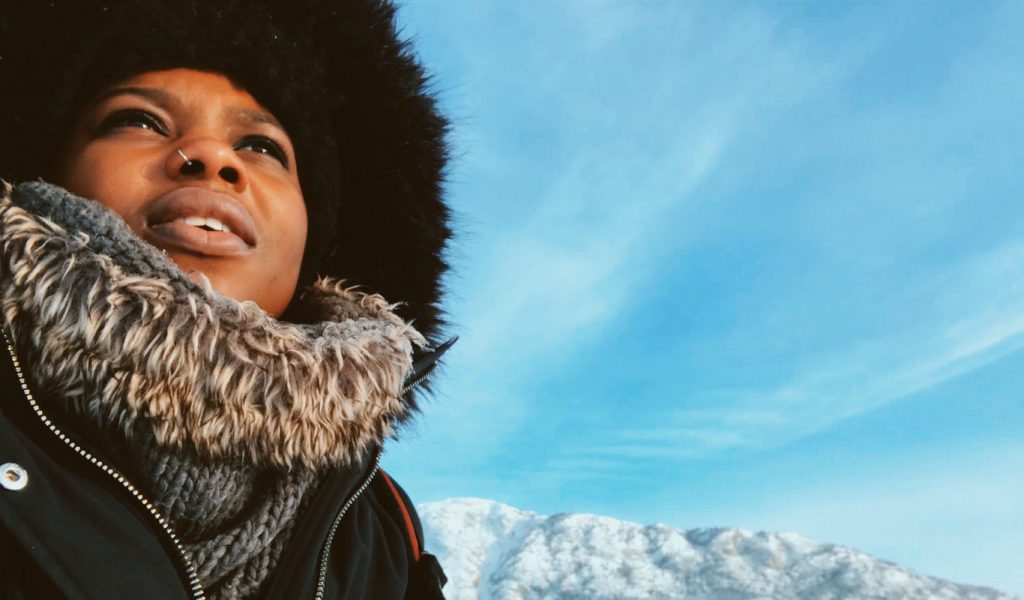 Black woman wearing a winter coat looks up to the sky in Yukon, Canada