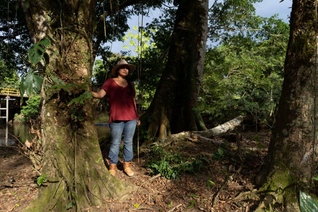 Woman with hat on in red shirt and jeans standing among trees in Colombia.