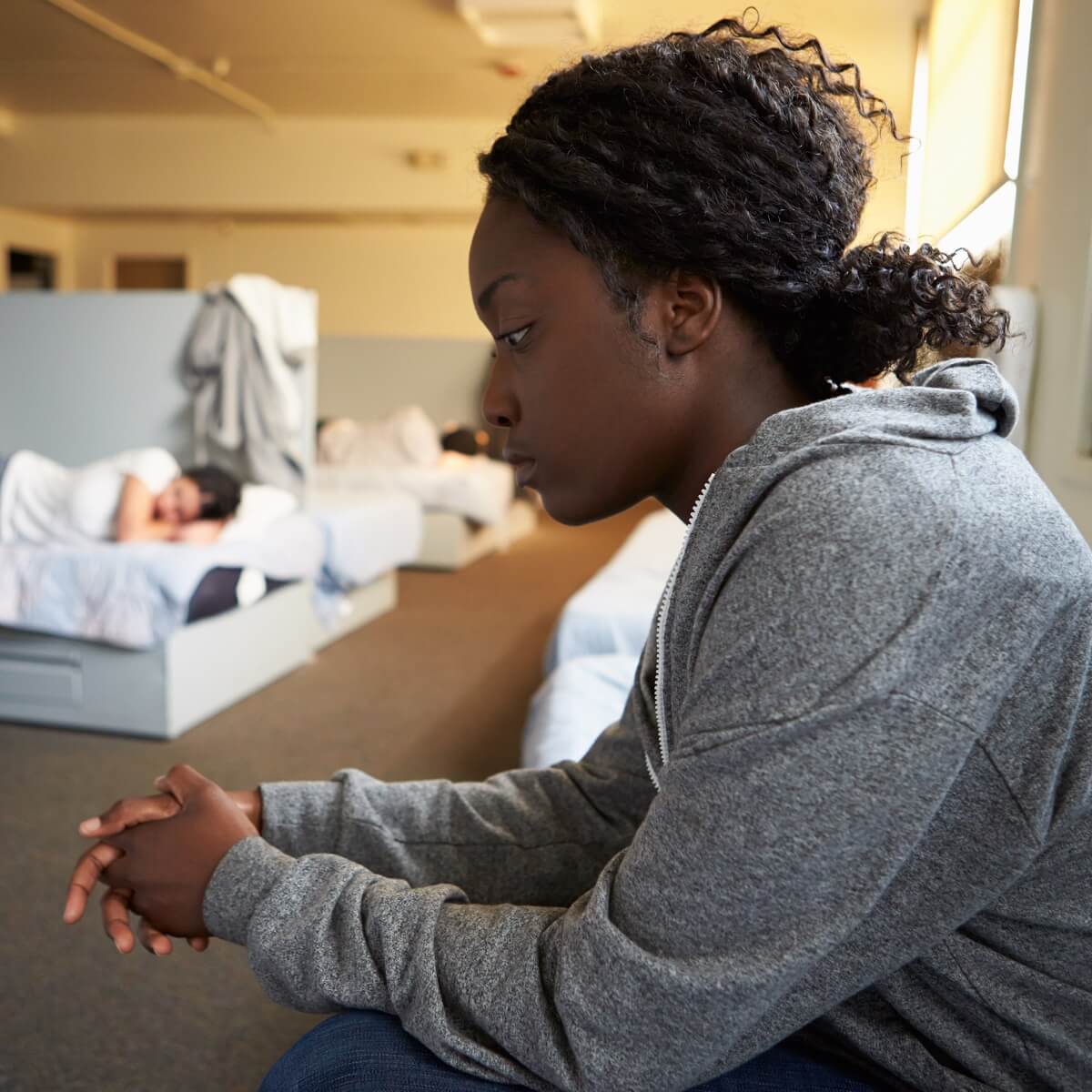 A woman sitting intensely in a room full of people laying in beds