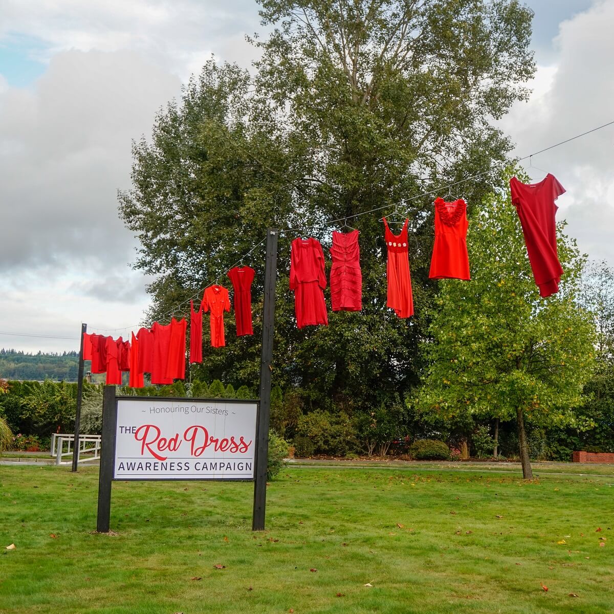 Several red dresses hang on a clothes line near a Red Dress Awareness Campaign sign