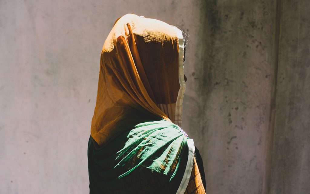 A woman facing a concrete wall with sunlight shining on her head