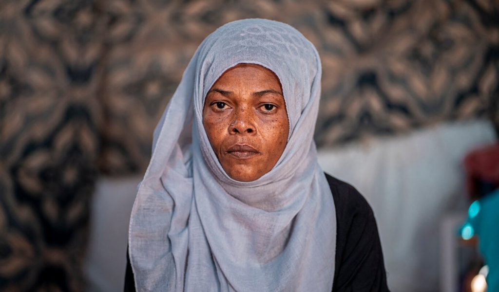 A Yemeni woman in a light blue headscarf looks directly at the camera with a serious look on her face.