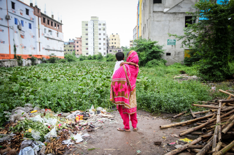 Woman in pink garment holding child looking off at collapsed building.