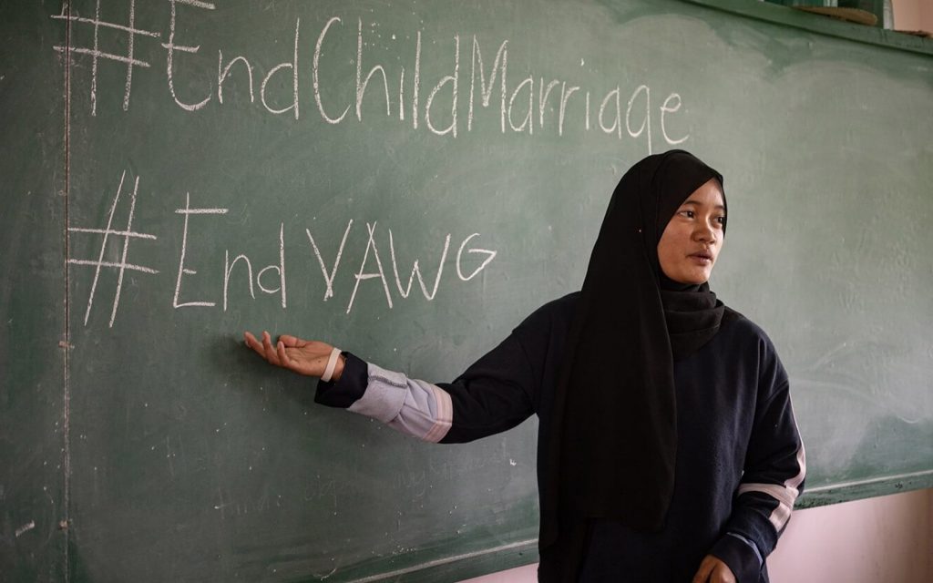 A woman in a classroom writing #EndChildMarriage on the chalkboard