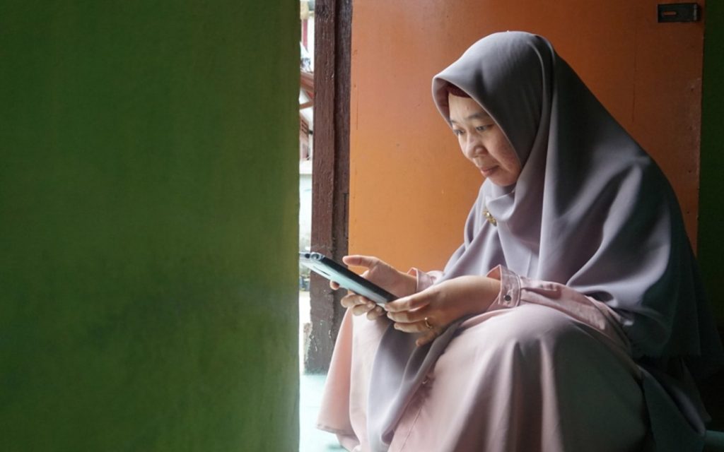 A woman sitting in a green and orange doorway looking at a mobile phone