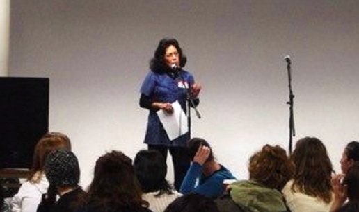 A middle-aged Guatemalan woman stands on stage with a piece of paper in her hand and speaks to an audience in 2005.