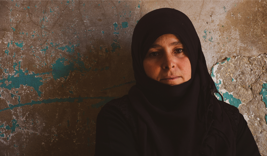 Woman in black hijab standing behind grey blue concrete wall.
