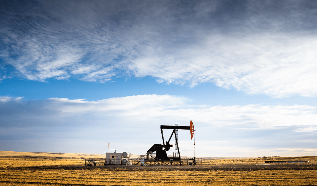 An industrial oil pump jack working on farm land under a morning sky in Rocky View County, Alberta, Canada.