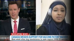 A capture from a television news report, with a male reporter who is wearing a red tie interviewing a woman wearing a navy blue hijab.