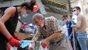 Lebanese volunteers with gloves and masks gather outside of buildings to clean streets and rebuild after the Port of Beirut explosion.