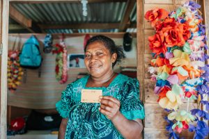 A smiling woman standing inside a room holds a card.