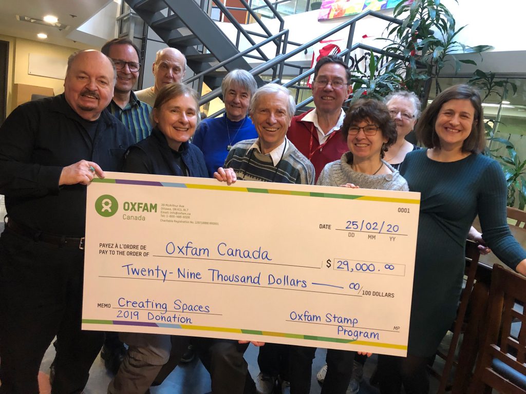 10 people stand in 2 rows on stairs holding a large cheque.