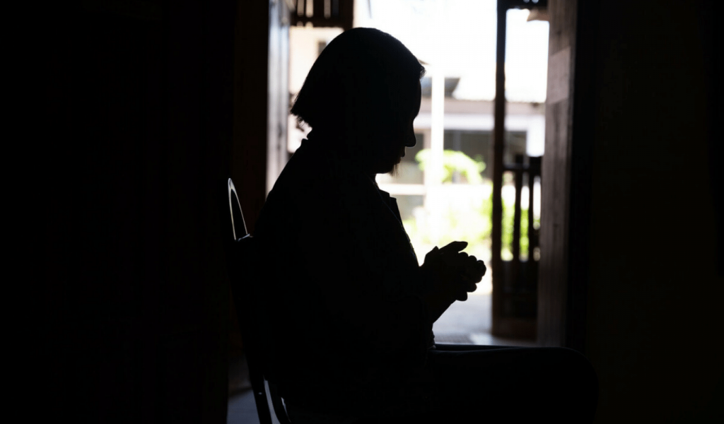 The contouring shape of a woman sitting down, holding her hands and looking at the floor.