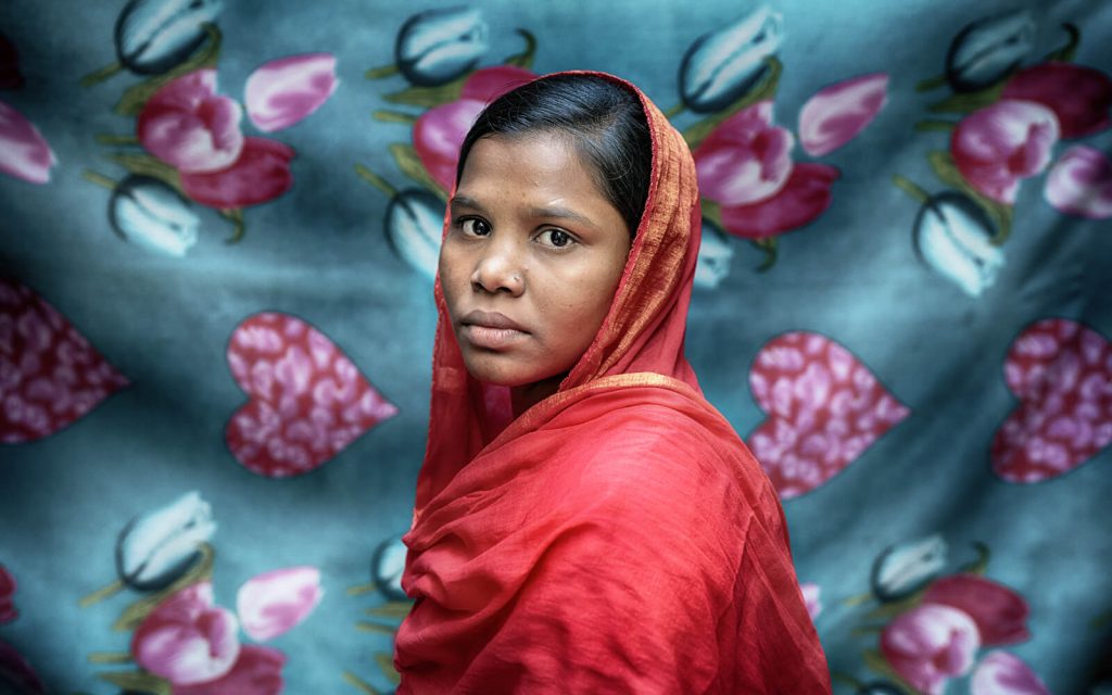 A woman in a red sari looks at the camera with a striking and serious expression.