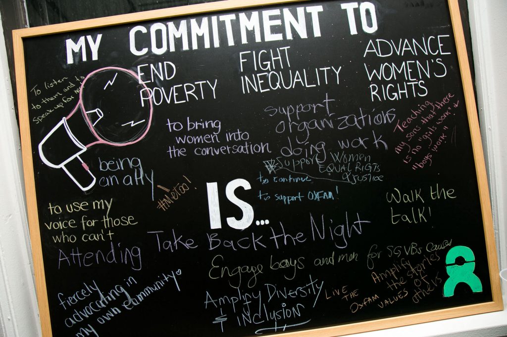 A large black chalkboard reads : 'My commitment to end poverty, fight inequality and advance women's rights is ...'. Handwritten answers to the prompt fill the chalkboard.