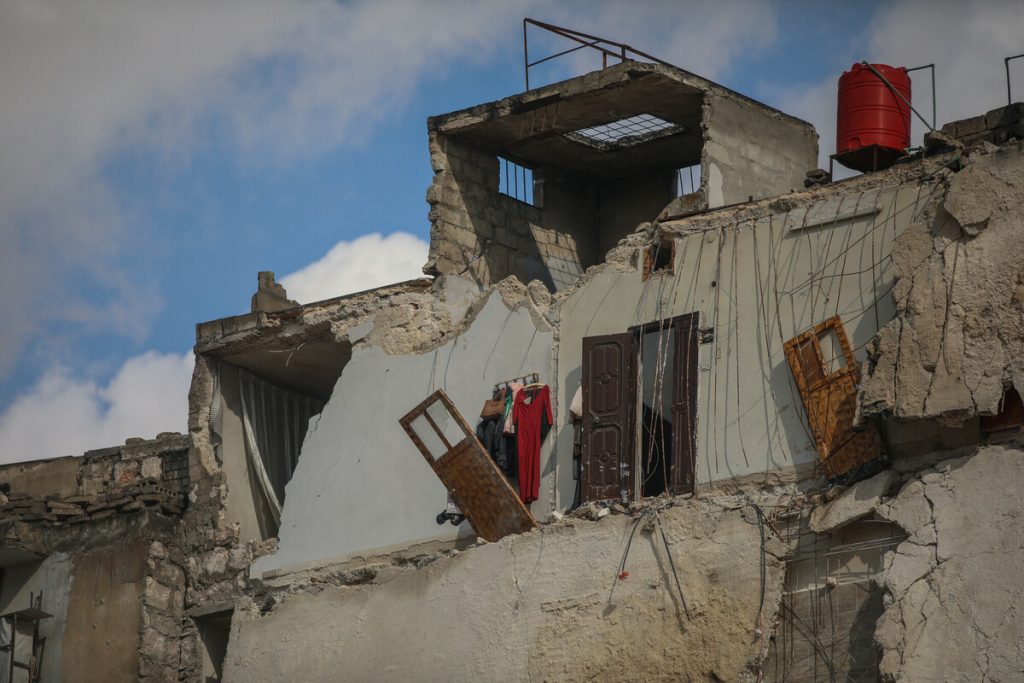 A partially collapsed second story of a concrete-built home, with colour floors still hanging in what used to be a bedroom's closet.