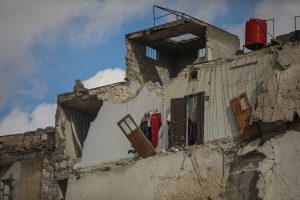 A partially collapsed second story of a concrete-built home, with colour floors still hanging in what used to be a bedroom's closet.
