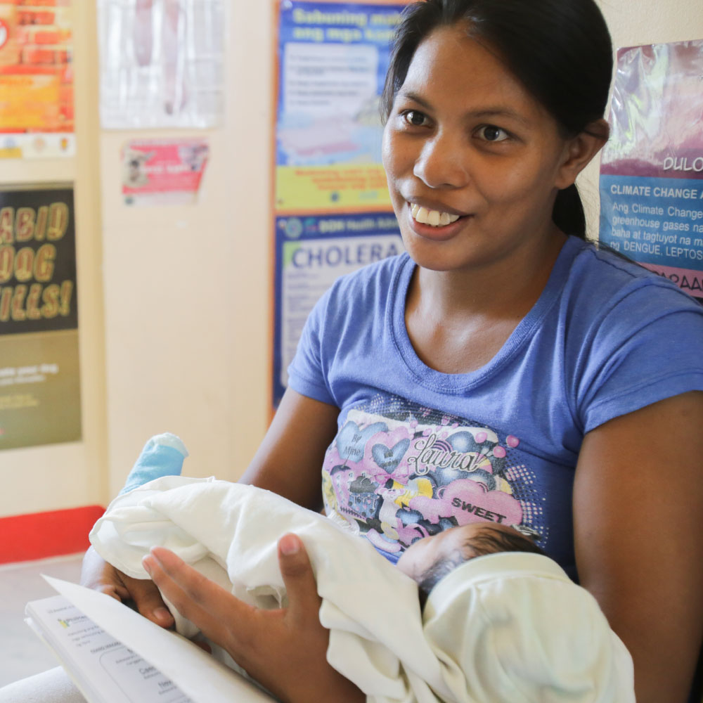 SexualReproductiveRights_Hero2 A smiling young mother holds a baby during a medical consultation.