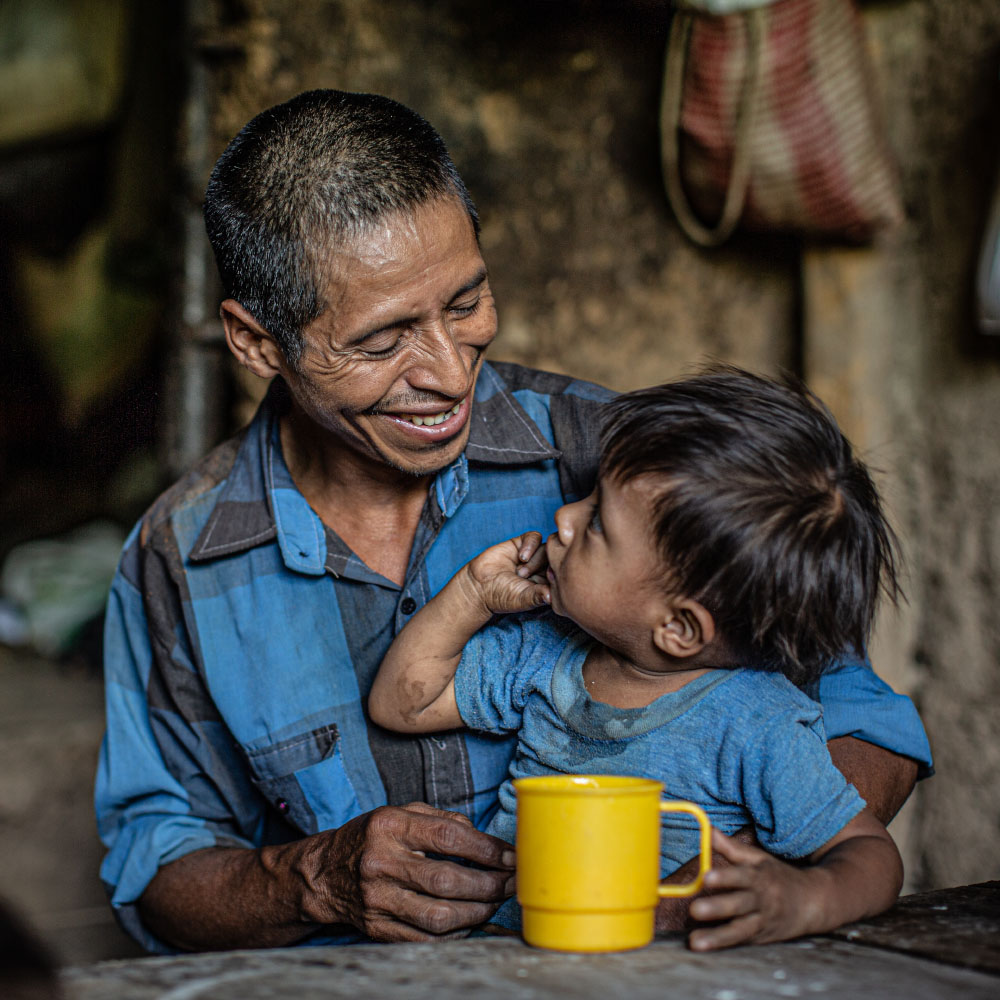 A father smiles at his son who is sitting on his lap.