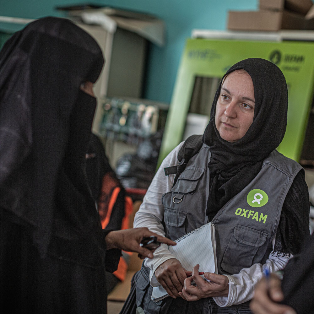 An Oxfam staff member listens to women speaking.
