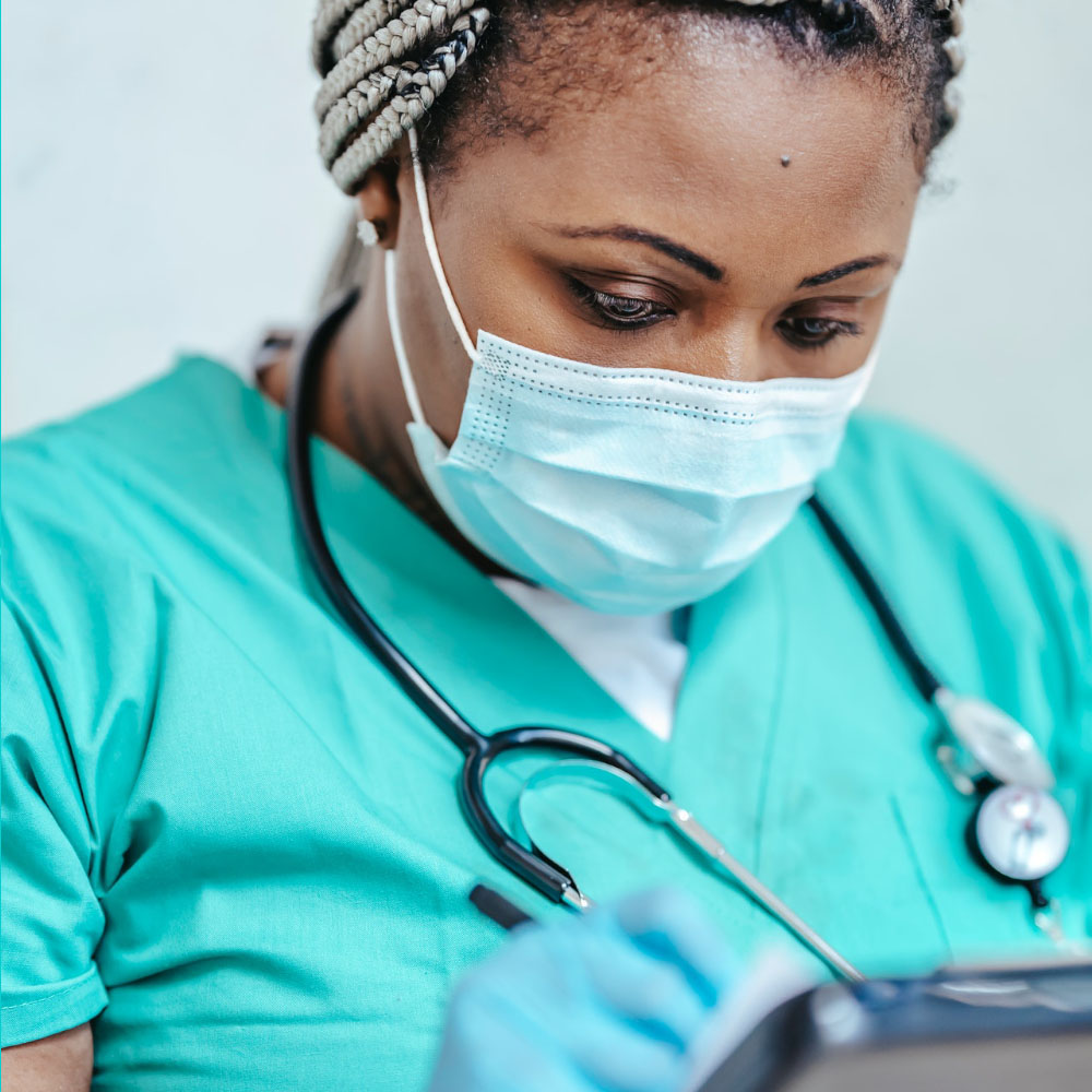 A masked nurse writes in her clipboard.
