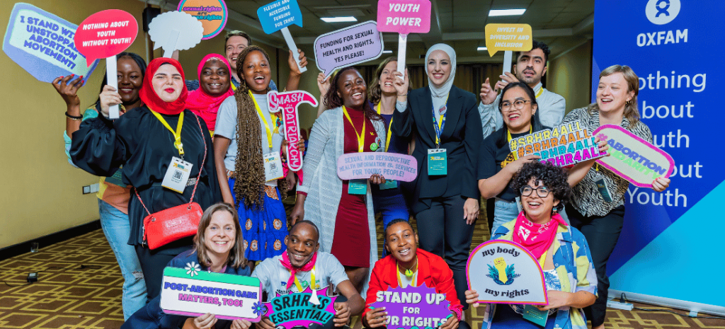 A group of young men and women smiling and holding signs with messages on sexual and reproductive health and rights.