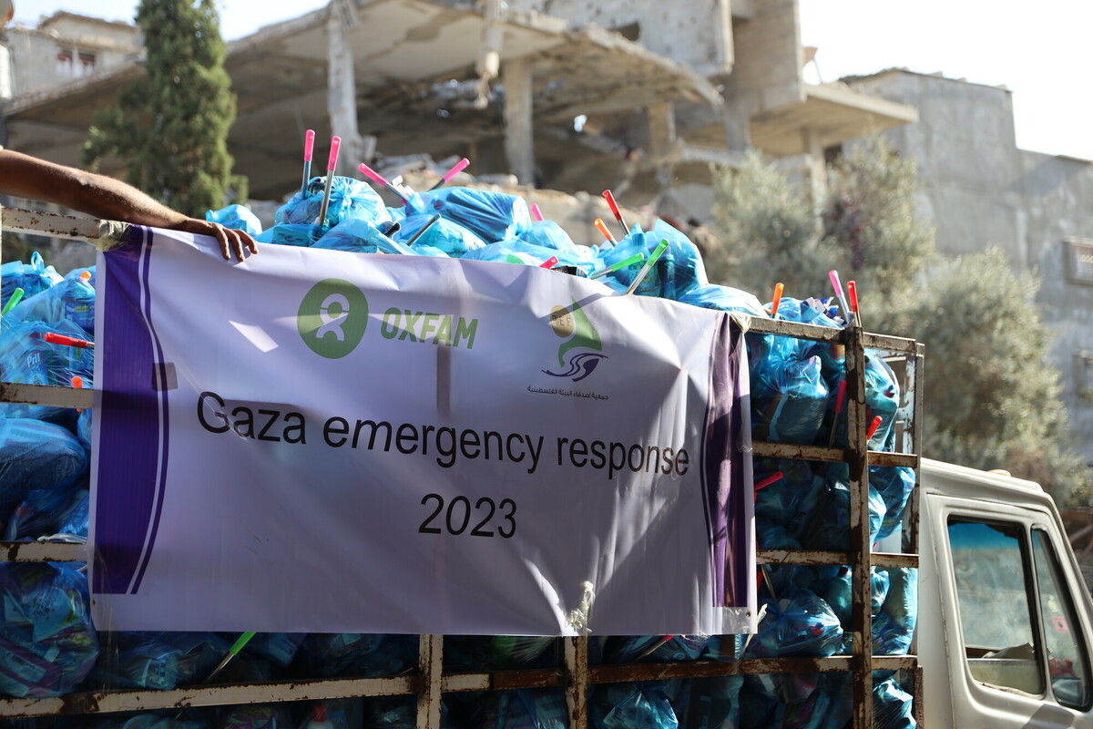 Close up of the back of a truck loaded with blue plastic bags containing hygiene kits. On the truck's side is a banner with Oxfam and partner logos on the top. Below them text that reads, "Gaza emergency response 2023."