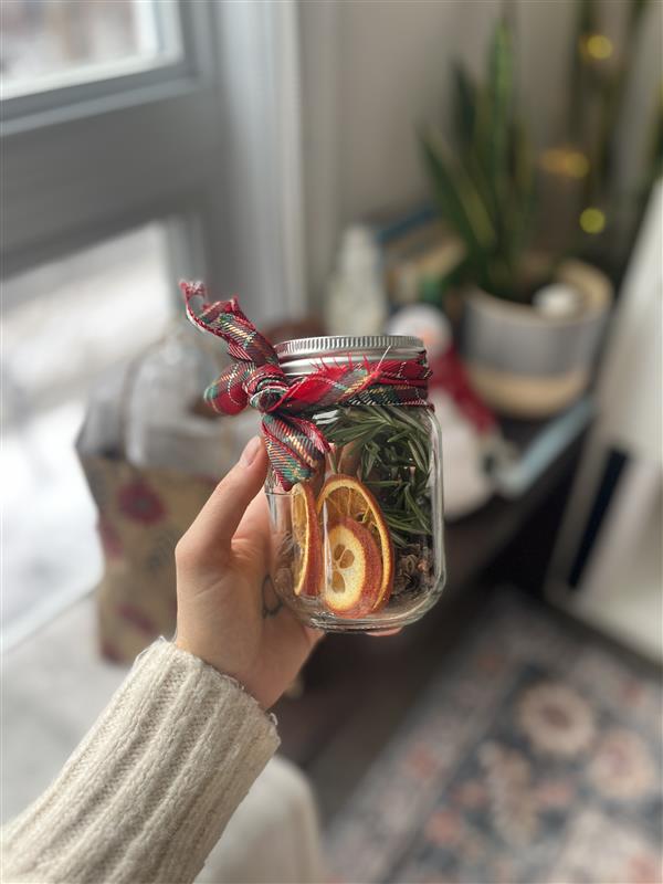 A holiday simmer pot kit, a mason jar filled with dried oranges, rosemary, cranberries, cinnamon sticks, and other holiday spices.