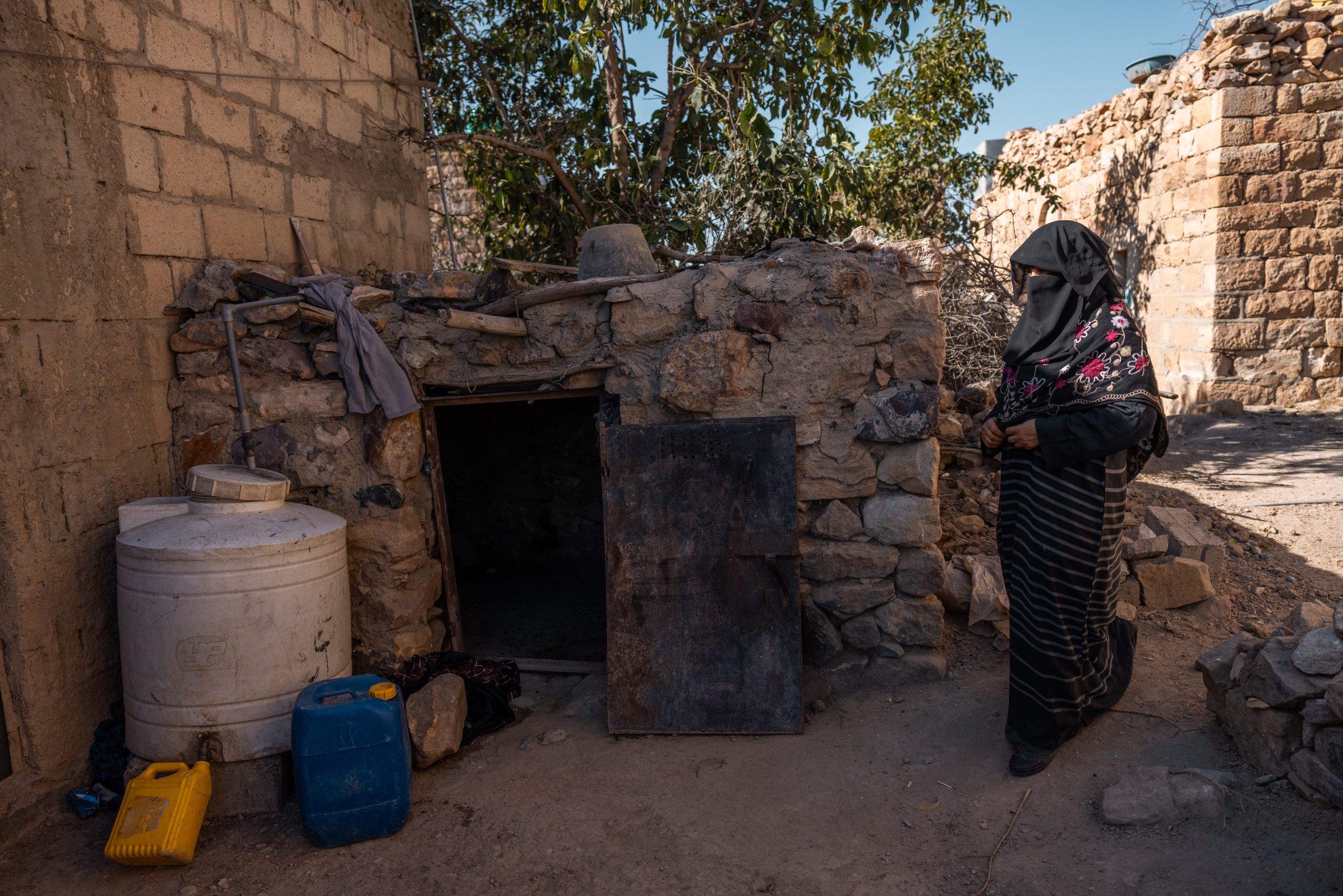 As Moniat steps inside her house, a water tank and several bottles filled with water stand beside the door, reminders of the days when every drop had to be carefully stored.