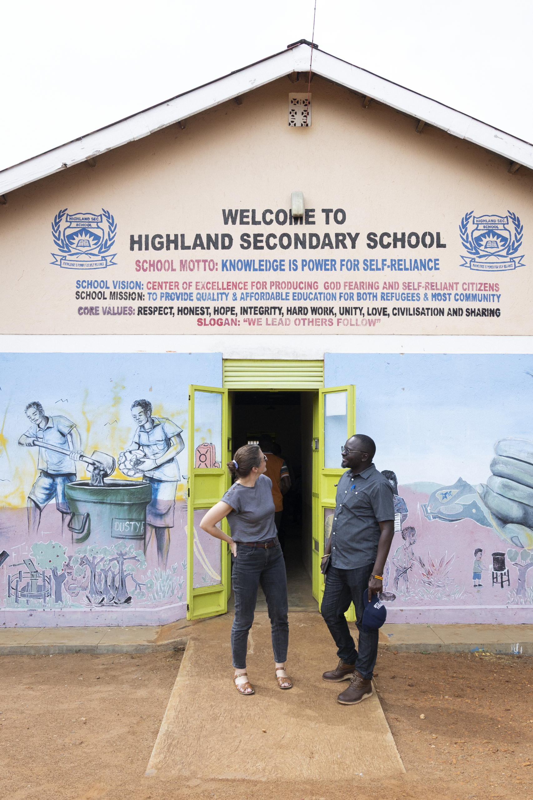 Lauren Ravon and Francis Shanty Odokorach, Oxfam in Uganda's Country Director, stand in front of Highland Secondary School. Photo: Mikaela Roberts / Oxfam