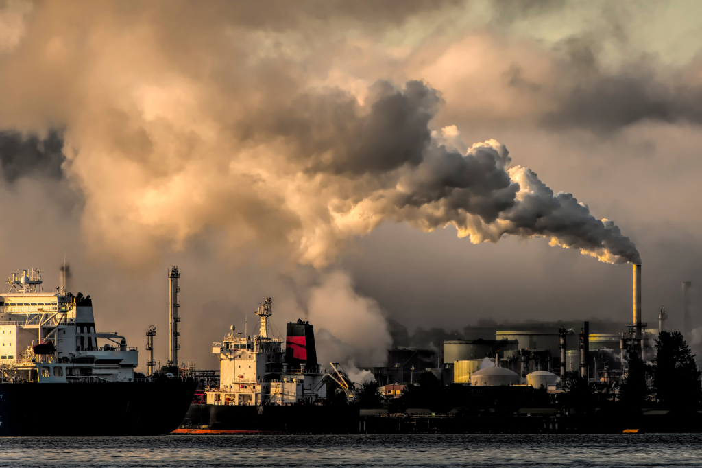 A dramatic capture of smokestacks releasing emissions over a waterfront, highlighting industrial pollution.