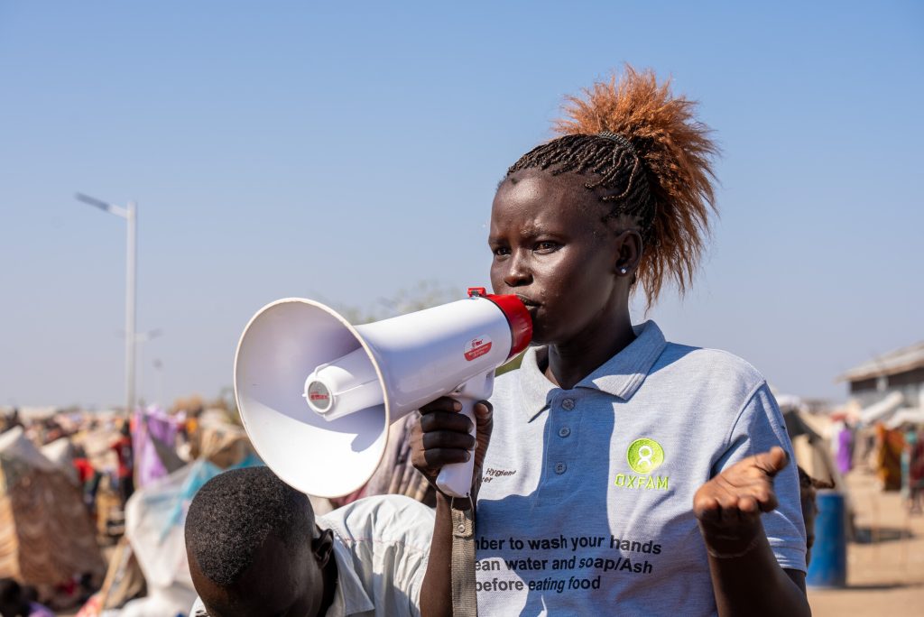 Woman wearing an Oxfam shirt talking on a megaphone.
