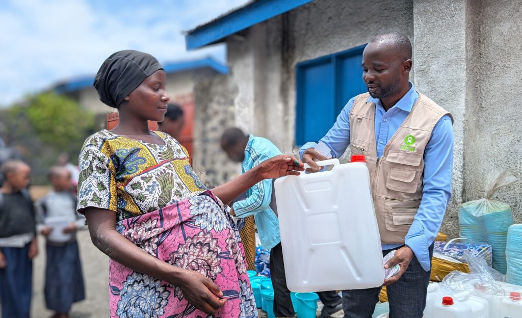 A man wearing an Oxfam vest handing a jerrycan to a pregnant woman.