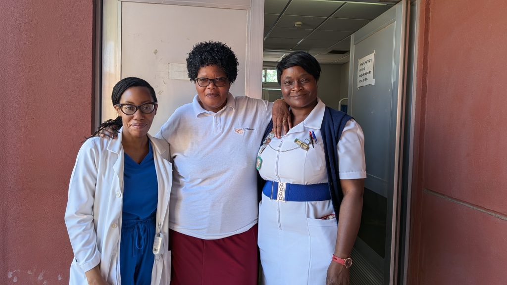 Three women standing and smiling at the camera.