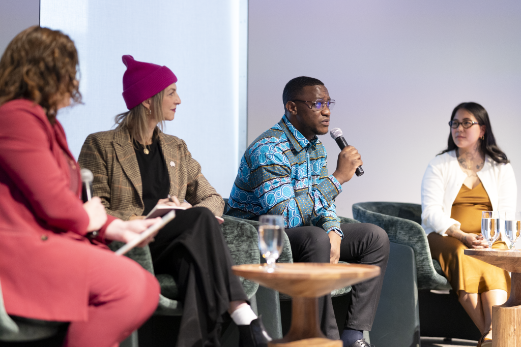 Three women and a man are speaking on a panel at a formal event.