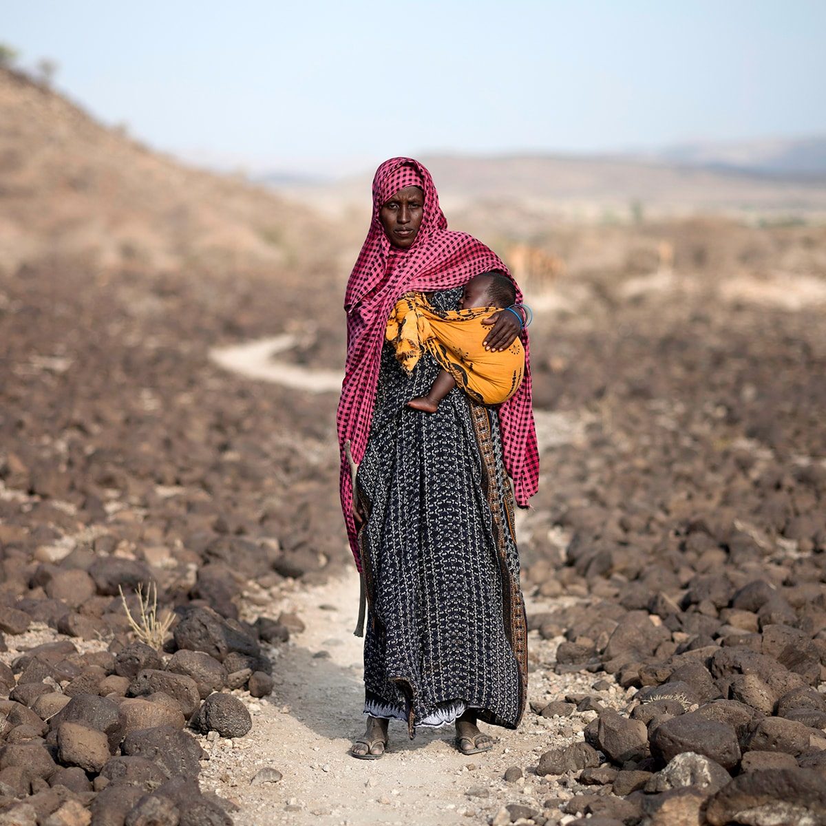 A woman carrying her small child in a cloth pouch.