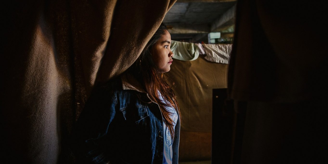 2019033 - Oxfam - Child Marriage - SRHR - 12 A woman stands behind a curtain in a bedroom, staring to your right side, not facing the camera.