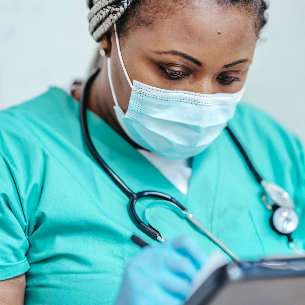 GenderJust_Impact1 A nurse wearing a face mask writes notes on a medical chart.