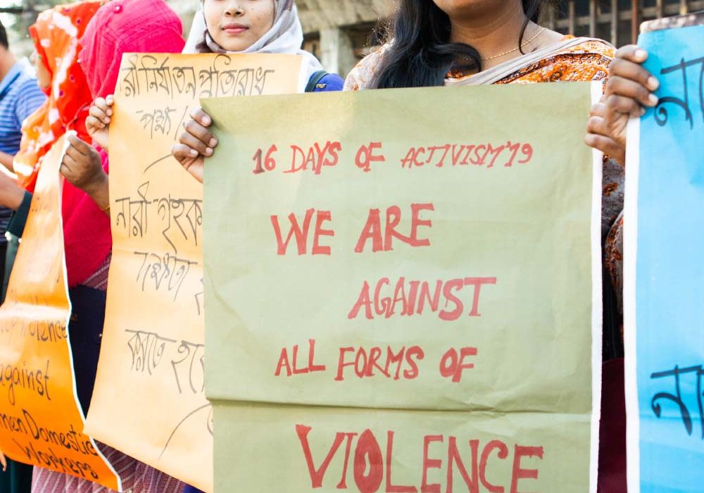 GenderJust_Securing1 A woman holds a poster that reads ‘We Are Against All Forms of Violence’.